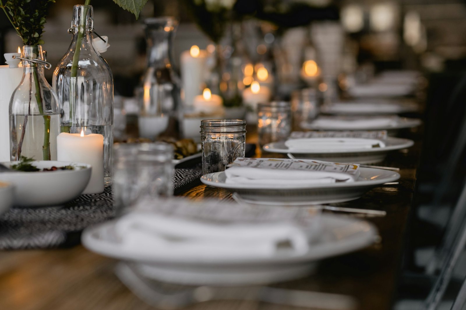 Long restaurant dining table set with white plates, candles and glass bottles